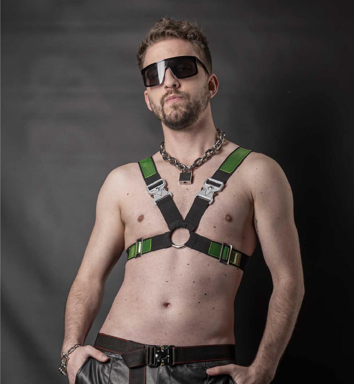 ein Mann mit Harness mit grünen Patches und massiver Halskette mit Schloss.