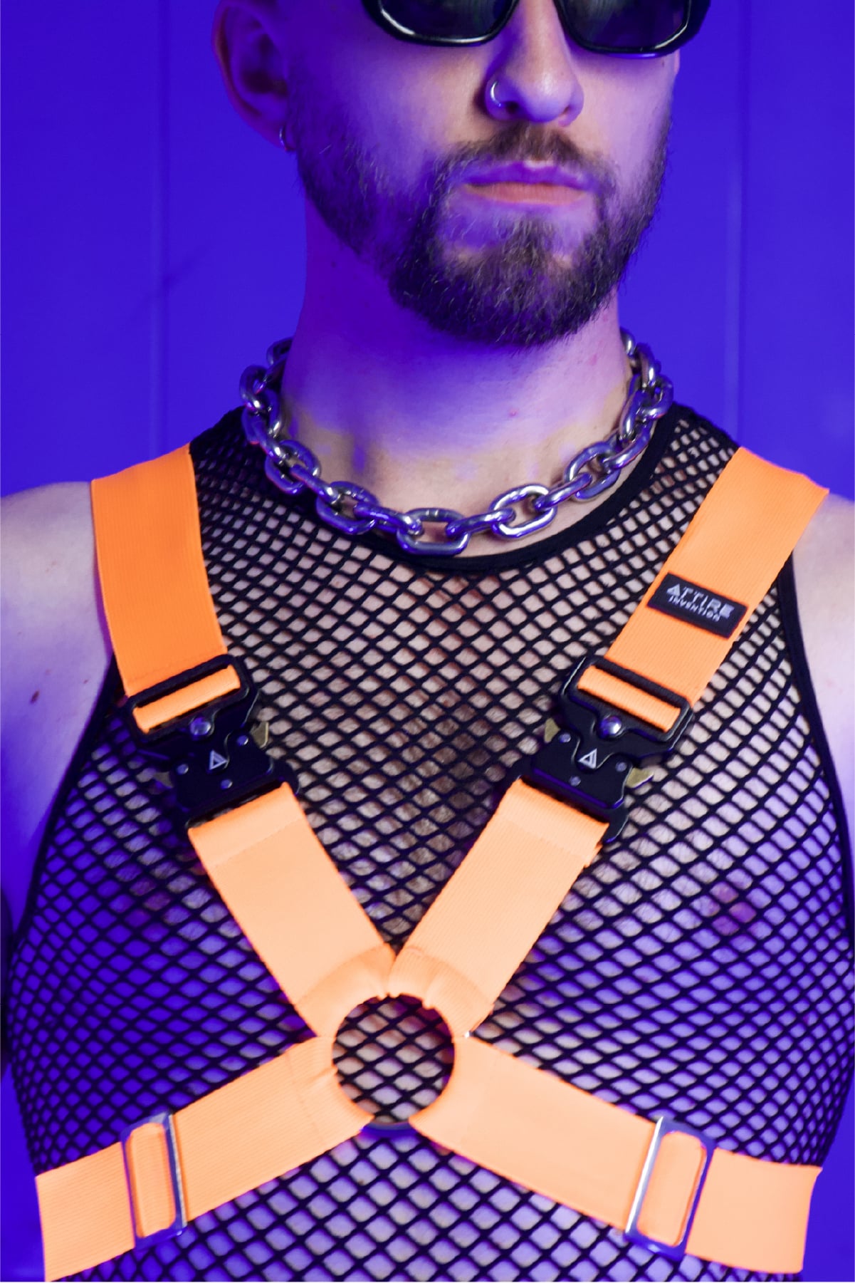 Ein Mann trägt einen Neon Orangenen Harness und ein Club Outfit.