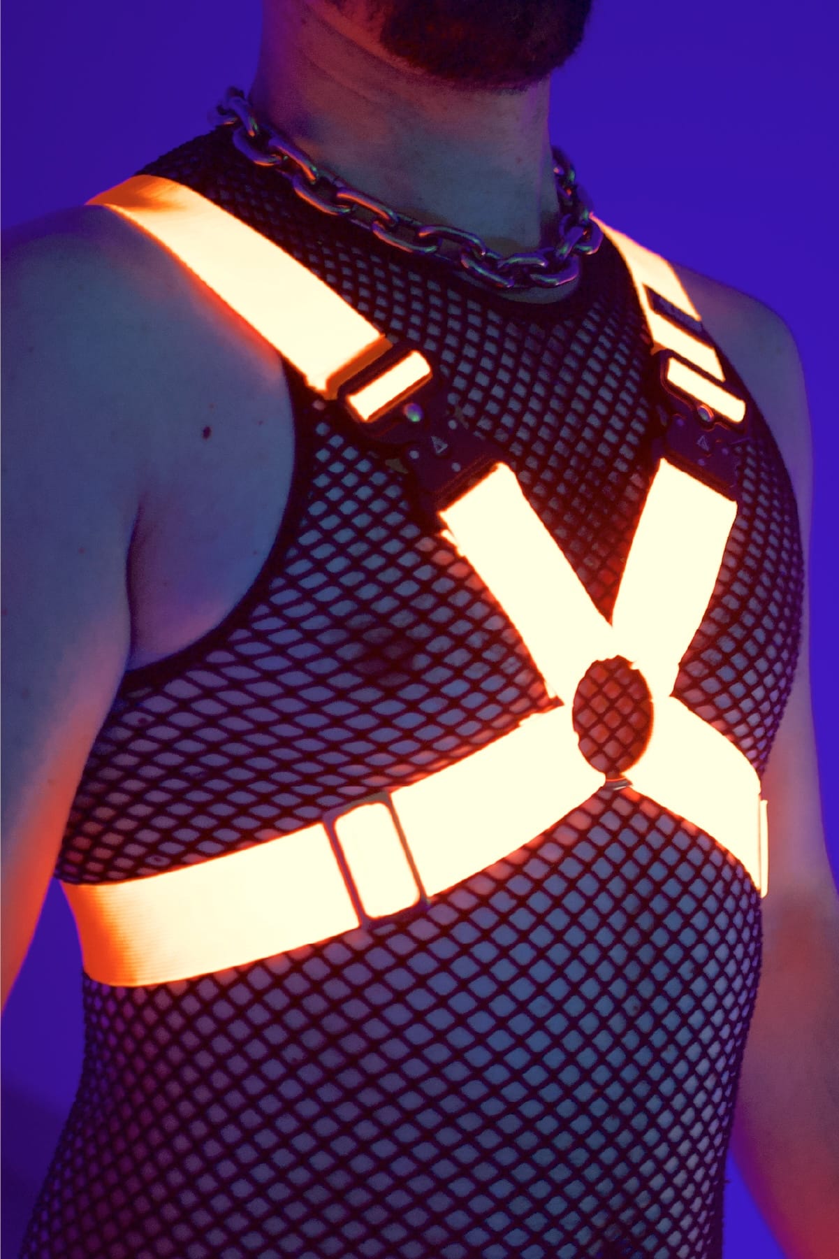 Ein Mann trägt einen Neon Orangenen Harness und ein Club Outfit.