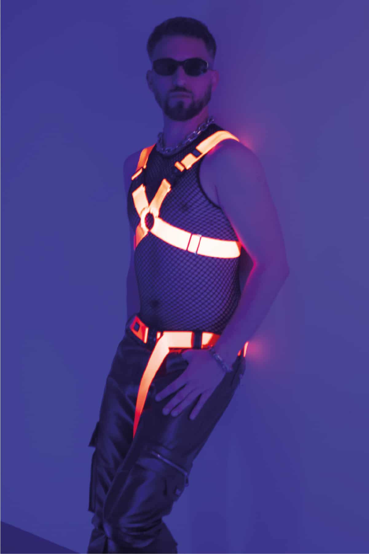 Ein Mann trägt einen Neon Orangenen Harness und ein Club Outfit.
